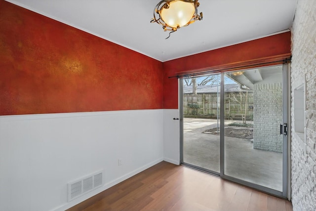 unfurnished room with wainscoting, visible vents, and wood finished floors