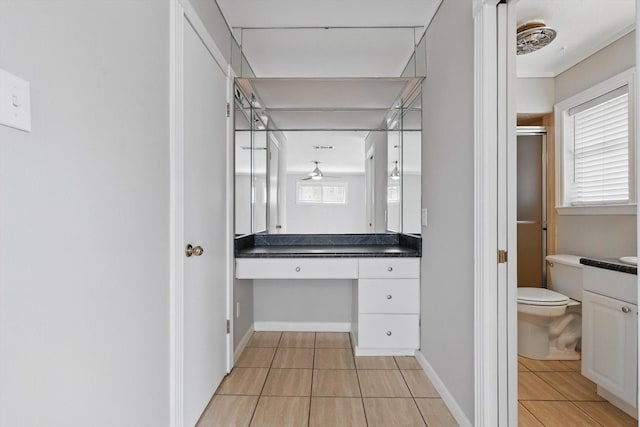 bathroom featuring tile patterned flooring, toilet, vanity, baseboards, and a shower with door