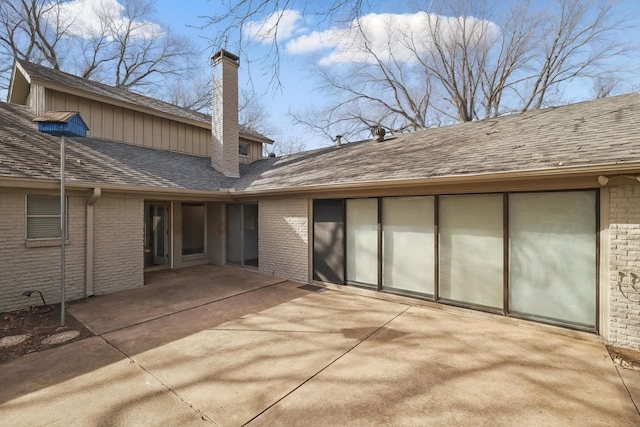 rear view of house with a patio area, a shingled roof, a chimney, and brick siding