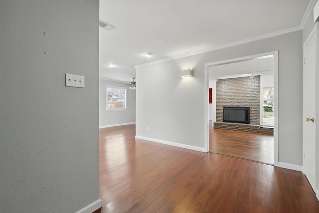 unfurnished living room with ornamental molding, a large fireplace, baseboards, and wood finished floors