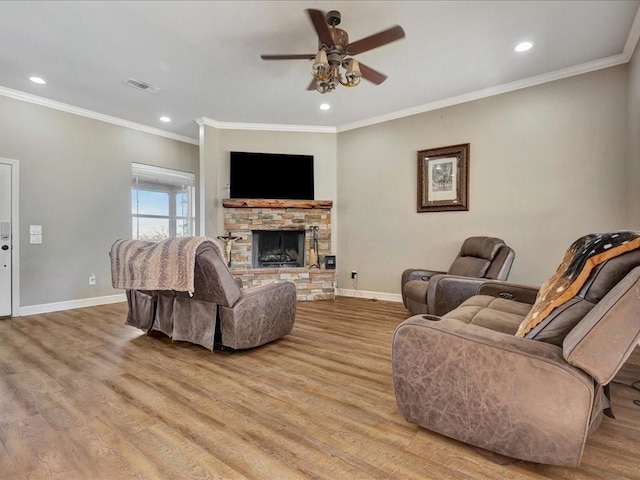 living room with crown molding, ceiling fan, a fireplace, and light wood-type flooring