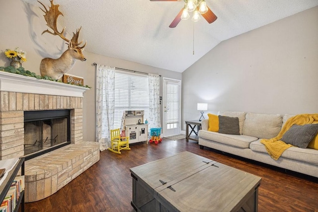 living room featuring dark wood-type flooring, ceiling fan, a textured ceiling, a brick fireplace, and vaulted ceiling