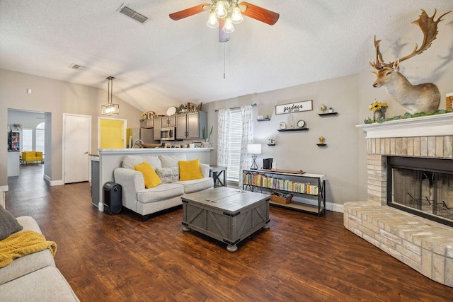 living room featuring dark wood-type flooring, ceiling fan, a textured ceiling, a brick fireplace, and vaulted ceiling