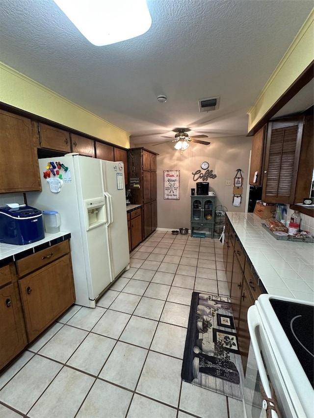 kitchen with light tile patterned floors, electric range, tile counters, ceiling fan, and white refrigerator with ice dispenser