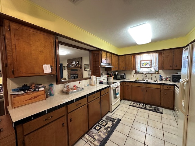 kitchen with tile countertops, sink, light tile patterned floors, a textured ceiling, and electric stove