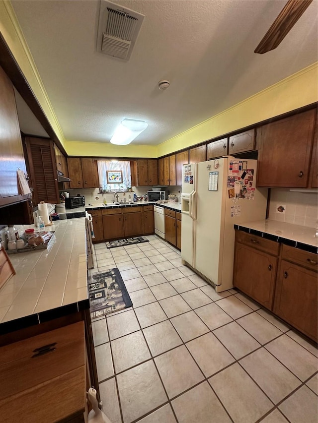 kitchen featuring white appliances, tile counters, ornamental molding, and light tile patterned flooring