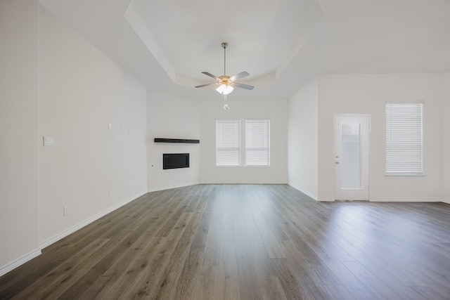 unfurnished living room with a raised ceiling, ceiling fan, and dark hardwood / wood-style floors