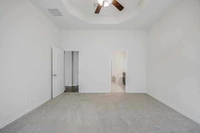 unfurnished bedroom with light colored carpet, ensuite bath, a tray ceiling, ceiling fan, and a high ceiling