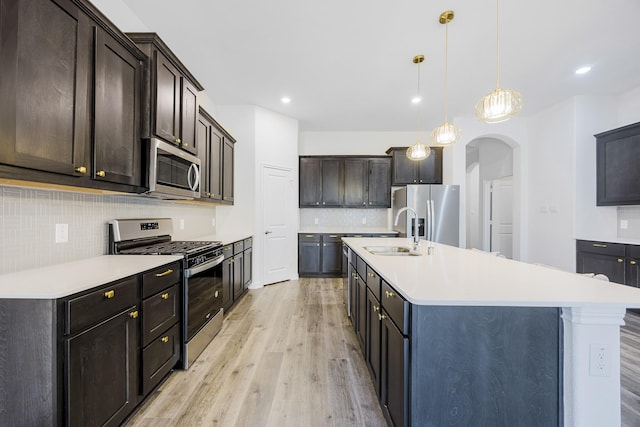 kitchen featuring light hardwood / wood-style flooring, sink, decorative light fixtures, stainless steel appliances, and a kitchen island with sink