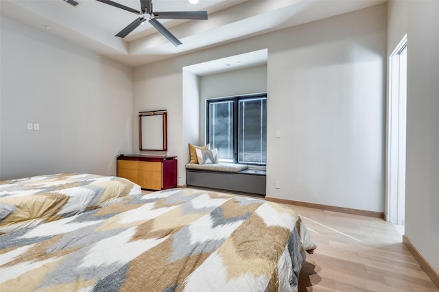 bedroom featuring ceiling fan, light hardwood / wood-style floors, and a tray ceiling