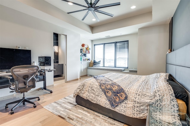 bedroom with light hardwood / wood-style floors, a raised ceiling, and ceiling fan