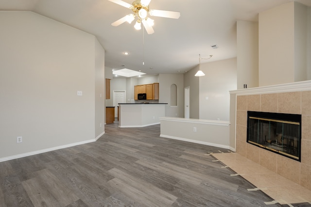 unfurnished living room with a tiled fireplace, wood-type flooring, and ceiling fan