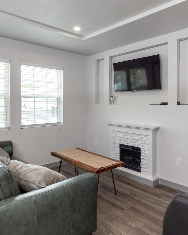 living room with a stone fireplace, dark wood-type flooring, and a textured ceiling