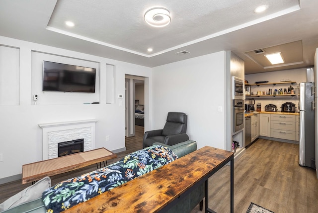 living room featuring a raised ceiling, a stone fireplace, hardwood / wood-style floors, and a textured ceiling