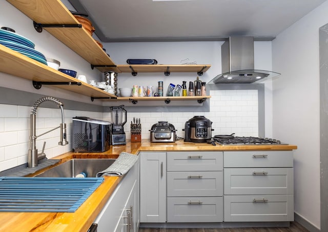 interior space featuring sink, wooden counters, backsplash, stainless steel gas cooktop, and island exhaust hood