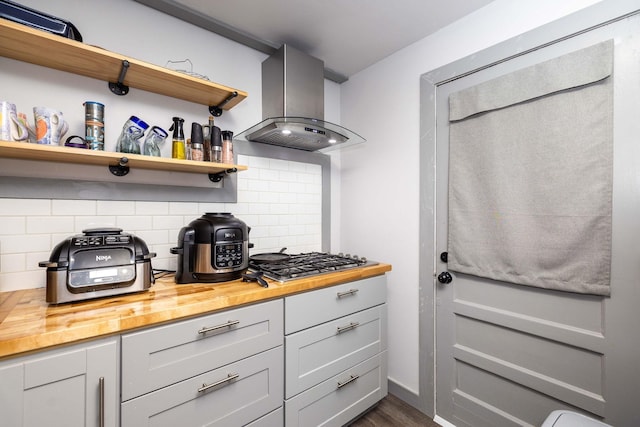 kitchen with wood counters, island range hood, dark hardwood / wood-style floors, stainless steel gas stovetop, and decorative backsplash