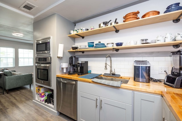 kitchen with butcher block countertops, wood-type flooring, sink, decorative backsplash, and stainless steel appliances