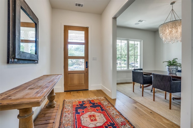 foyer entrance with a chandelier, light wood-type flooring, visible vents, and baseboards