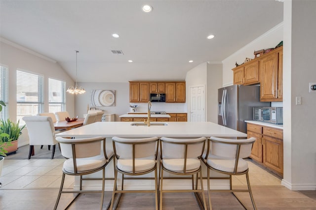 kitchen with stainless steel appliances, light countertops, decorative backsplash, a sink, and an island with sink