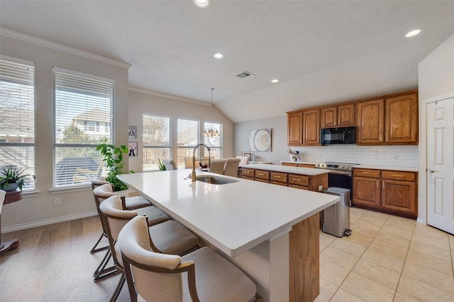 kitchen with a center island with sink, visible vents, brown cabinetry, a sink, and black microwave