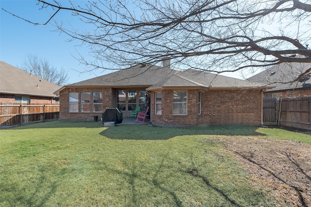 back of house featuring brick siding, a chimney, a fenced backyard, and a lawn