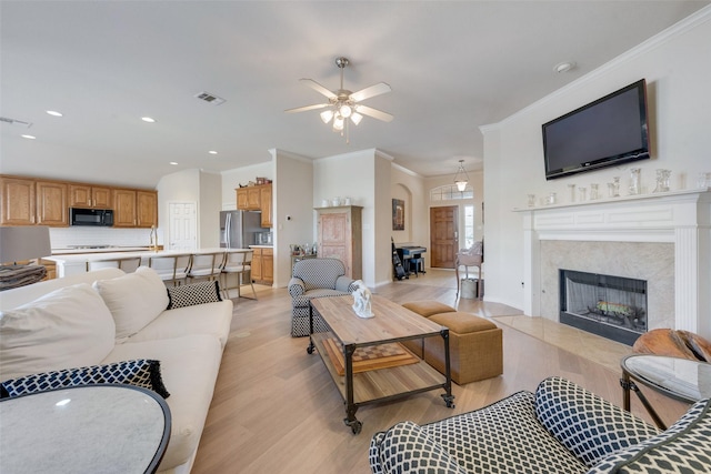 living room with a fireplace, visible vents, light wood-style flooring, ornamental molding, and baseboards