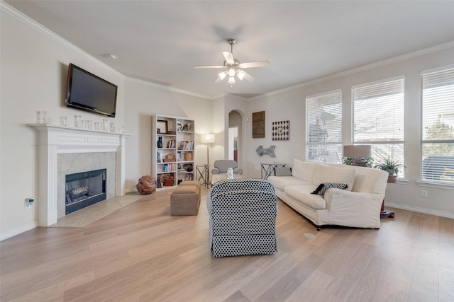 living room featuring light wood-style floors, a fireplace, arched walkways, and ornamental molding