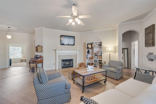 living room featuring arched walkways, ceiling fan, a premium fireplace, ornamental molding, and light wood-type flooring