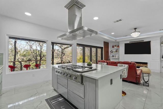 kitchen featuring a kitchen island, gray cabinetry, island exhaust hood, stainless steel gas cooktop, and a tray ceiling