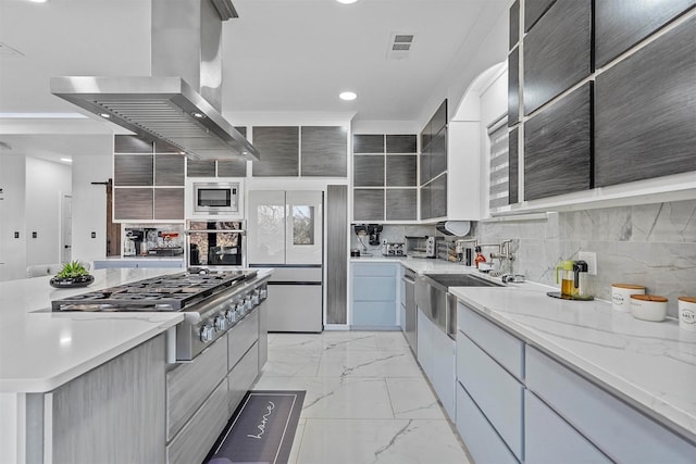 kitchen with island range hood, sink, backsplash, light stone counters, and stainless steel appliances