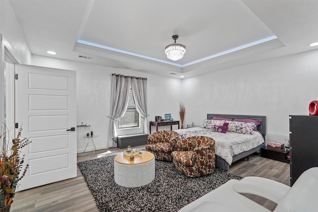 bedroom featuring a tray ceiling, wood-type flooring, and a chandelier