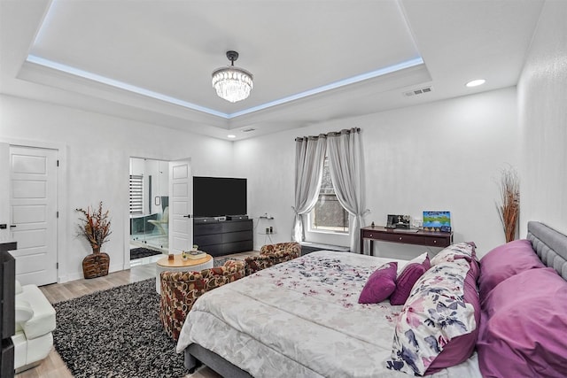 bedroom with an inviting chandelier, ensuite bathroom, a raised ceiling, and light wood-type flooring