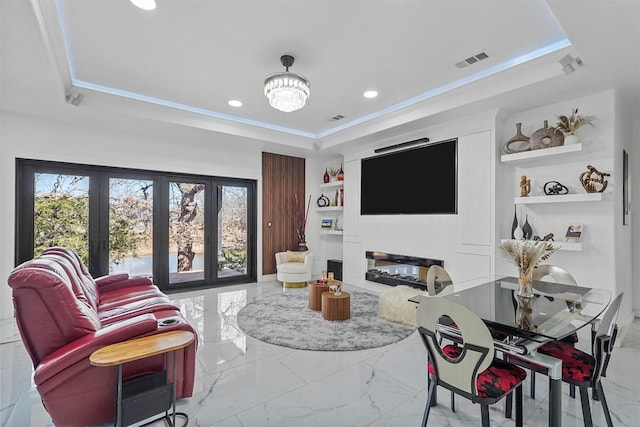 living room with crown molding, a tray ceiling, built in features, and a chandelier