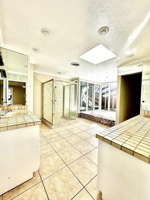 kitchen featuring light tile patterned floors, sink, a skylight, a textured ceiling, and tile countertops