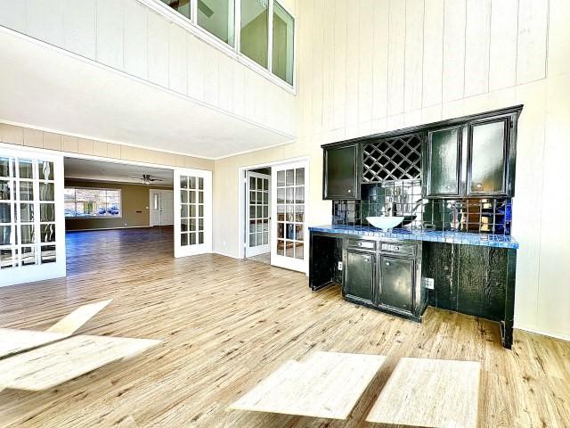 bar featuring a towering ceiling, french doors, dark stone counters, and light wood-type flooring