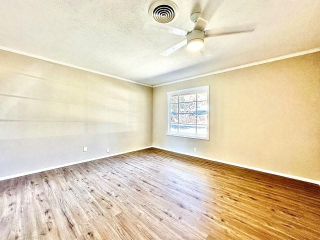 empty room featuring hardwood / wood-style flooring, ceiling fan, ornamental molding, and a textured ceiling