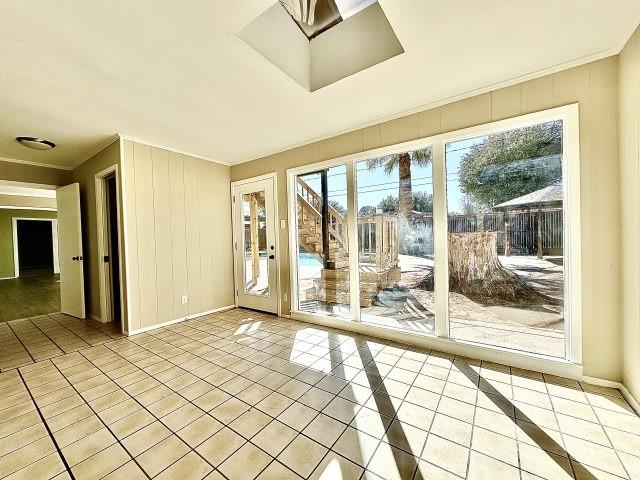 interior space featuring light tile patterned flooring, crown molding, and a skylight