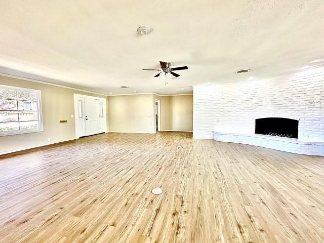 unfurnished living room featuring crown molding, a fireplace, light hardwood / wood-style floors, and ceiling fan