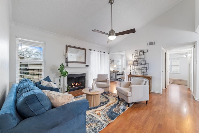 living room featuring visible vents, ceiling fan, a textured ceiling, wood finished floors, and a warm lit fireplace