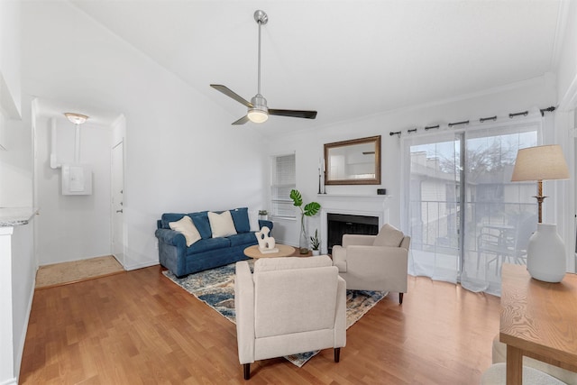 living room featuring a ceiling fan, light wood-type flooring, vaulted ceiling, and a fireplace