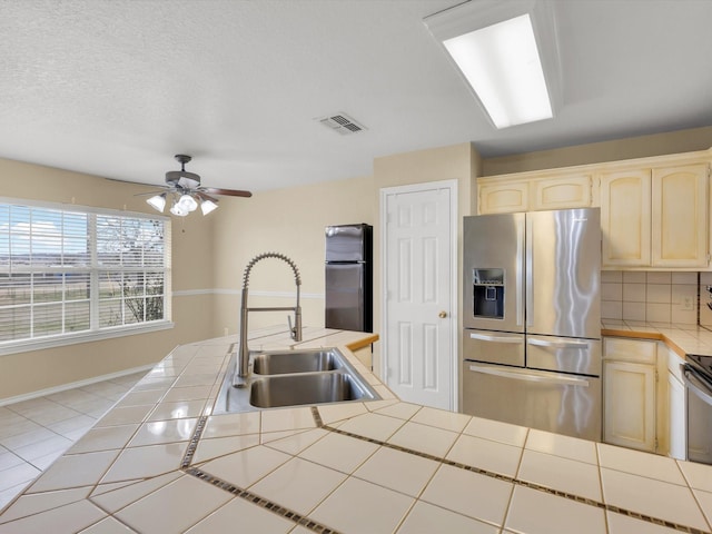 kitchen featuring refrigerator, sink, decorative backsplash, tile counters, and stainless steel refrigerator with ice dispenser