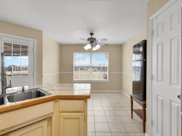 kitchen featuring sink, light tile patterned floors, ceiling fan, tile counters, and a textured ceiling