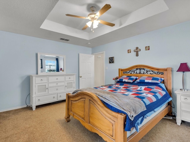 carpeted bedroom with a raised ceiling and ceiling fan