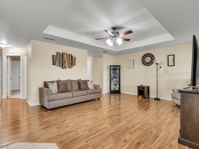 living room featuring ceiling fan, a tray ceiling, light hardwood / wood-style flooring, and a textured ceiling