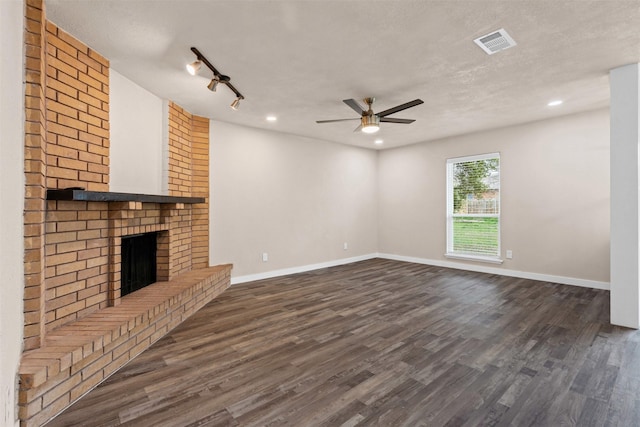 unfurnished living room featuring a textured ceiling, dark wood-style flooring, a brick fireplace, and visible vents