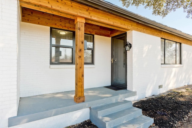 property entrance with crawl space, brick siding, and covered porch