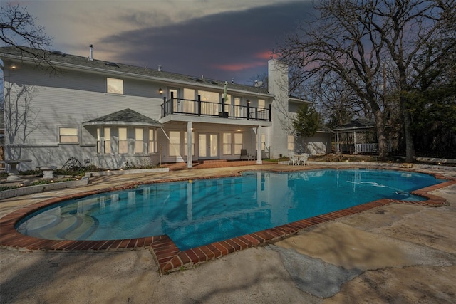 pool at dusk featuring an outdoor pool, french doors, and a patio