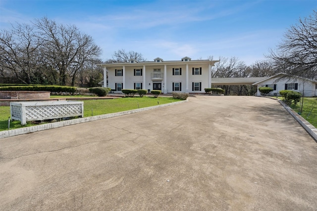 neoclassical home featuring driveway, a carport, covered porch, and a front yard