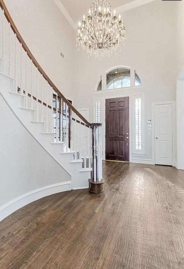 entryway with hardwood / wood-style floors, crown molding, a chandelier, and a towering ceiling