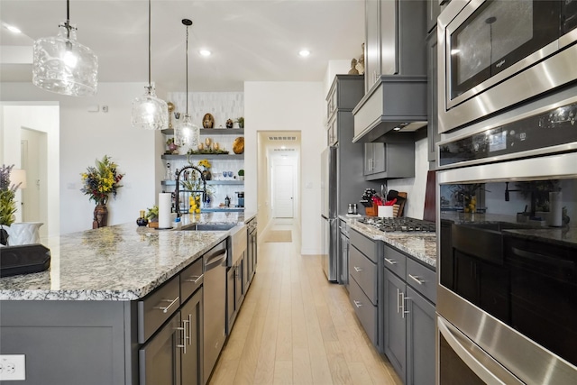 kitchen featuring sink, appliances with stainless steel finishes, hanging light fixtures, light stone counters, and a large island with sink